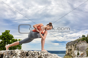Attractive woman is practicing yoga on the rock against beautiful landscape.
