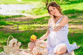 Young pregnant girl in a white sarafan on a plaid in a park at a