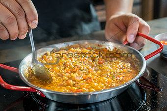 Chef is cooking paella with spoon, close up
