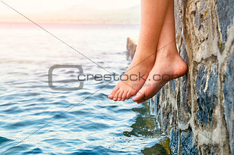 Bare girl's feet dangling from the stone jetty