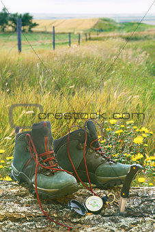 Hiking boots with knife and compass on log in field 