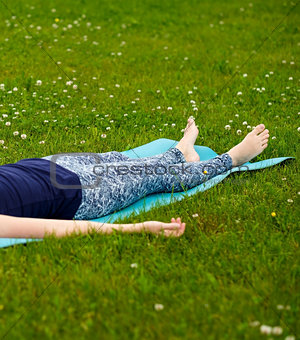 Girl doing yoga, meditating, Shavasana or corpse position in park on green grass