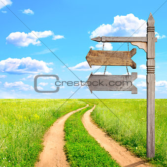 Rural summer landscape with dirt road and old wooden signboard 