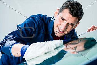 Cheerful young worker polishing car with soft microfiber mitt