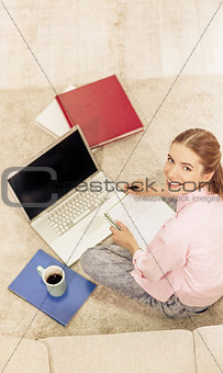 Top view of smiling young girl studying sitting on carpet.