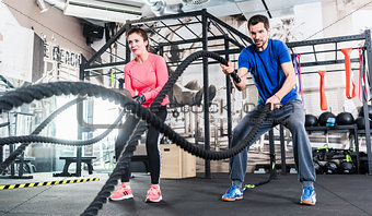 Woman and man in gym functional training with battle rope