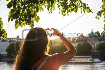 Woman hands showing shape of a heart on sunset, young woman travel alone, love concept.