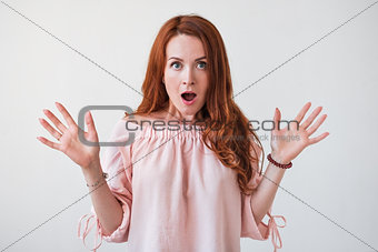 Portrait young woman with long curly red hair looking excited holding her mouth opened isolated on white wall.