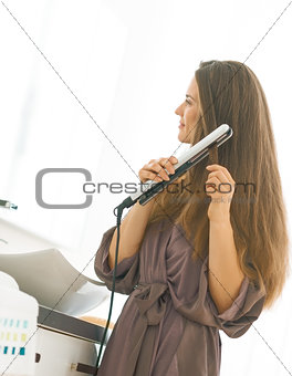 Young woman using hair straightener in bathroom