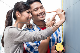 Young indonesian couple measuring walls in new apartment