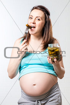 Hungry pregnant woman with a jar of pickled cucumbers against a 
