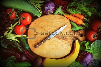 Fresh raw vegetable ingredients for healthy cooking or salad making with wooden cutting board in center, top view, copy space. Diet or vegetarian food concept