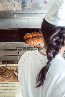 Baker getting fresh bread with shovel out of oven