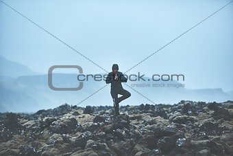 Woman hiker stands in yoga pose on volcanic Lava fields on background of mountains of Iceland.