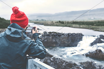 a woman photographing a waterfall on phone