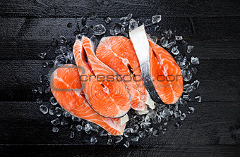 Salmon steaks on ice on black wooden table top view