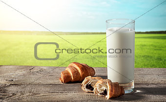 Glass of milk on rustic table with croissants