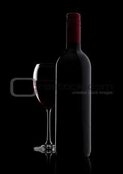 Glass of red wine with bottle with shape on black