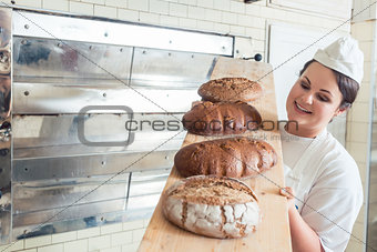 Baker woman presenting bread on board in bakery