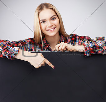 Young Smiling teenager blond girl hold black blank paper and shows on it.