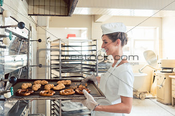 Baker woman getting bakery products out of oven