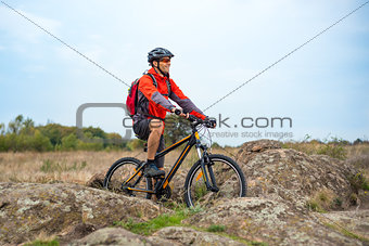 Happy Cyclist in Red Resting on the Bike on Rocky Trail. Adventure Sport and Travel Biking Concept.