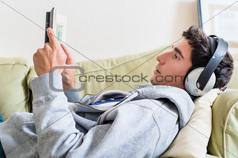 Relaxed young man lying down on the couch while reading a book a