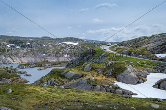 Scenic Norwegian landscape with rocks, lake and curved mountain road.