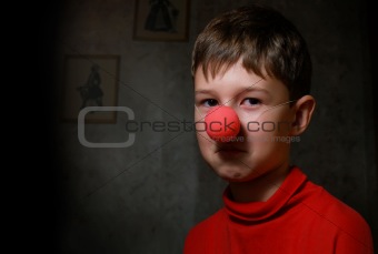 The upset boy with clown's nose in dark room