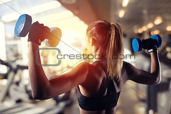 Athletic girl trains biceps at the gym