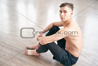 Handsome ballet dancer sitting on the floor and resting