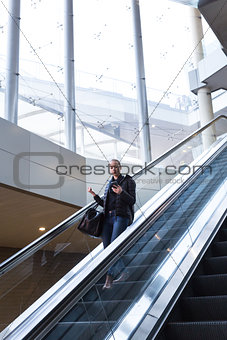 Businesswoman with large black bag and mobile phone descending on escalator.