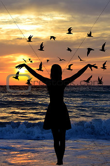 Young woman silhouette with birds on the seaside