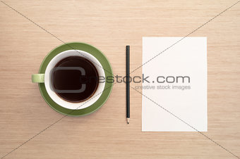 A green cup of coffee on the background of a table and a white shee and pencil