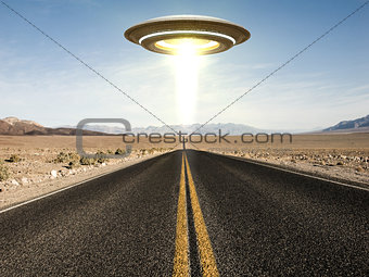 ufo flying over an empty desert road