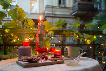 Romantic dinner table on balcony with candles, chocolates and fruits