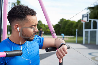 Young man at outdoor gym checking fitness app on smartwatch
