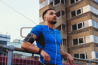 Male runner takes a break leaning on fence in urban setting
