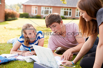 Teenage Students Sitting Outdoors And Working On Project