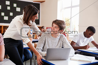 Teacher Helping Male Pupil Using Computer In Classroom