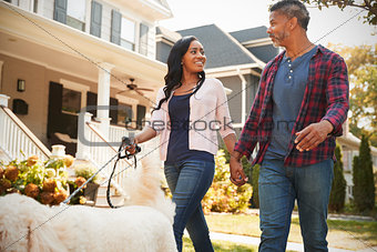 Couple Walking Dog Along Suburban Street