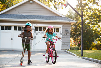 Sister With Brother Riding Scooter And Bike On Driveway At Home
