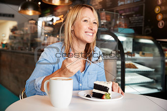 Woman In Coffee Shop Sitting At Table Eating Slice Of Cake