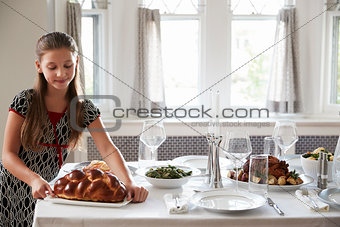 Girl placing challah bread on a table for Shabbat meal