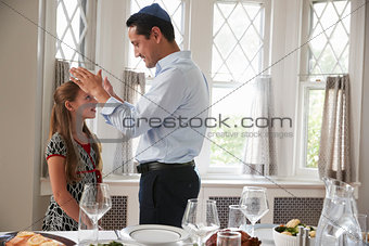 Jewish father blesses daughter by table set for Shabbat meal