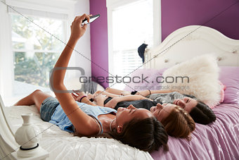 Teenage girl taking a selfie with two friends lying on a bed