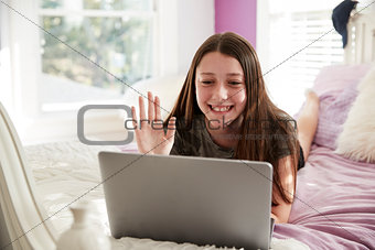 Teen girl lying on bed making a video call with laptop