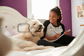 Young teen girl doing homework on her bed with pet dog
