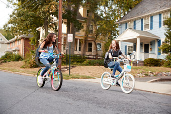 Two teen girlfriends ride past on bikes in a quiet street