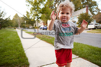 Toddler boy standing in the street making a face to camera